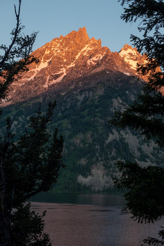 Het eerste licht van de ochtendzon op Symmetry Spire en Mount Saint John boven Jenny Lake, Grand Tetons, Wyoming
