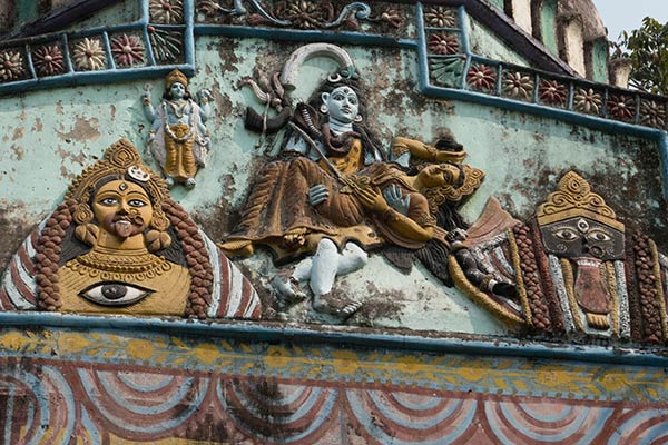 Shiva draagt ​​het lichaam van Shakti terwijl hij de wilde dans van Tandava door het universum doet. Snijwerk op de buitenmuur van de tempel, Bhabanipur Shakti Pitha